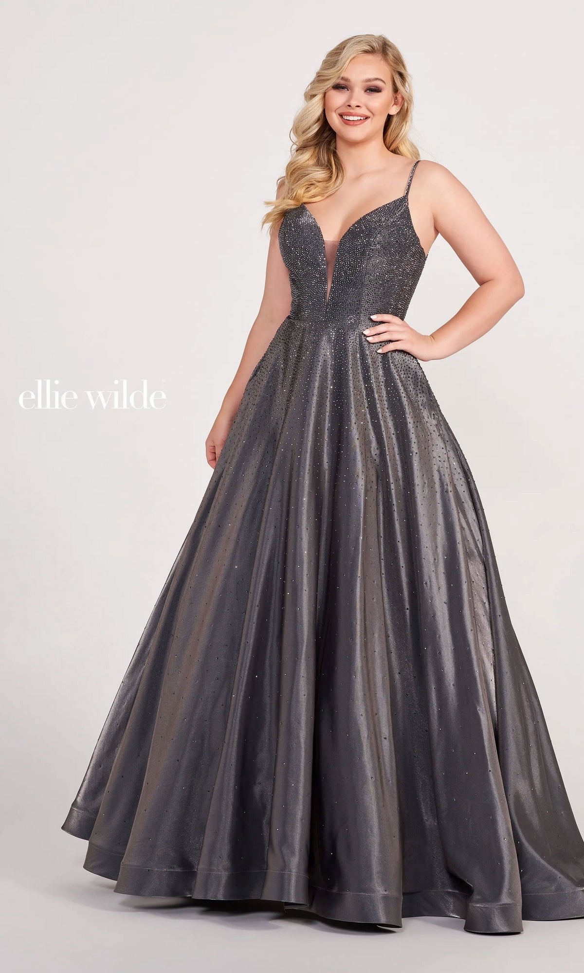 A woman wears the Ellie Wilde Ew121005, a sleeveless, floor-length metallic gray beaded prom ball gown with a deep V-neckline and subtle sparkling embellishments, standing against a plain background.